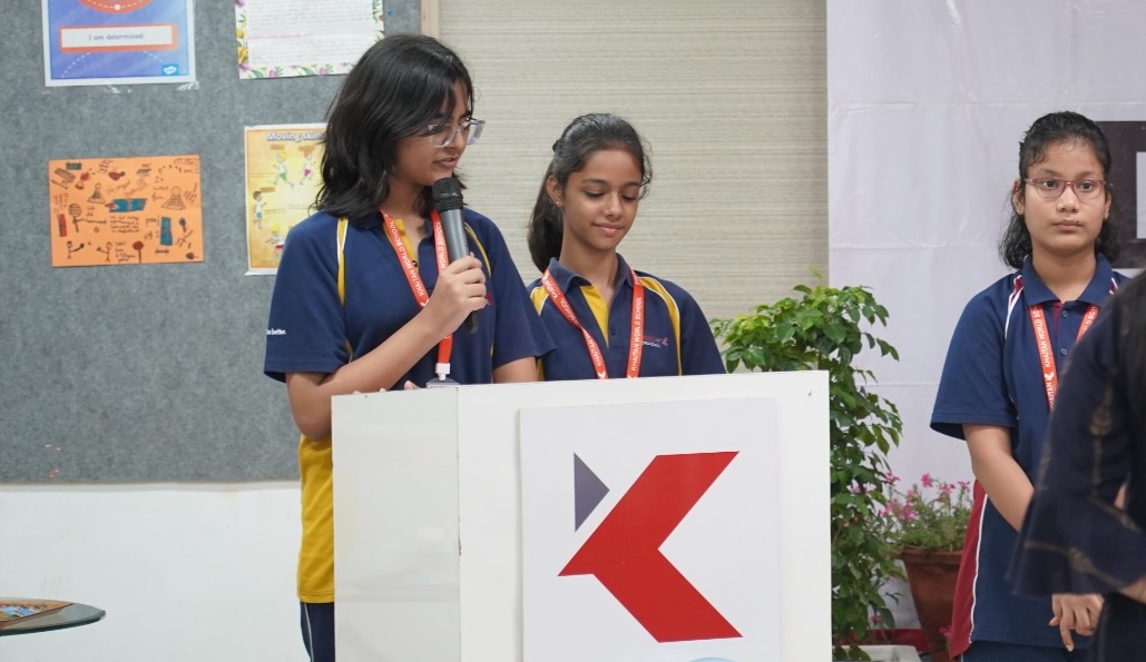 Khaitan World School students speaking at a lectern during a school assembly